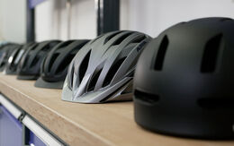 Mehrere Fahrradhelme in verschiedenen Farben und Designs sind in einer Reihe auf einer Werkbank angeordnet. 