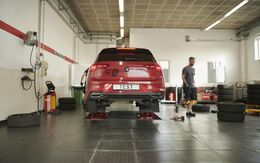 Sommerreifentest - Auto in Werkstatt ist auf der Hebebühne, rechts im Bild sieht man einzelne Reifen, Werkzeug und einen Mann.