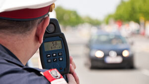 Ein Polizist misst mit einer Laserpistole die Geschwindigkeit eines schwarzen Autos.