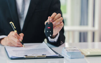 Jemand unterschreibt etwas und hält mit der anderen Hand einen Autoschlüssel