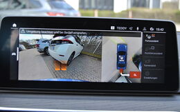 Screen von einem Einparkassistenten im Cockpit, darauf sichtbar das Heck von zwei Autos am Parkplatz.