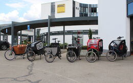 Sechs einspurige Elektro-Lastenfahrräder sind vor einem Gebäude aufgestellt.
