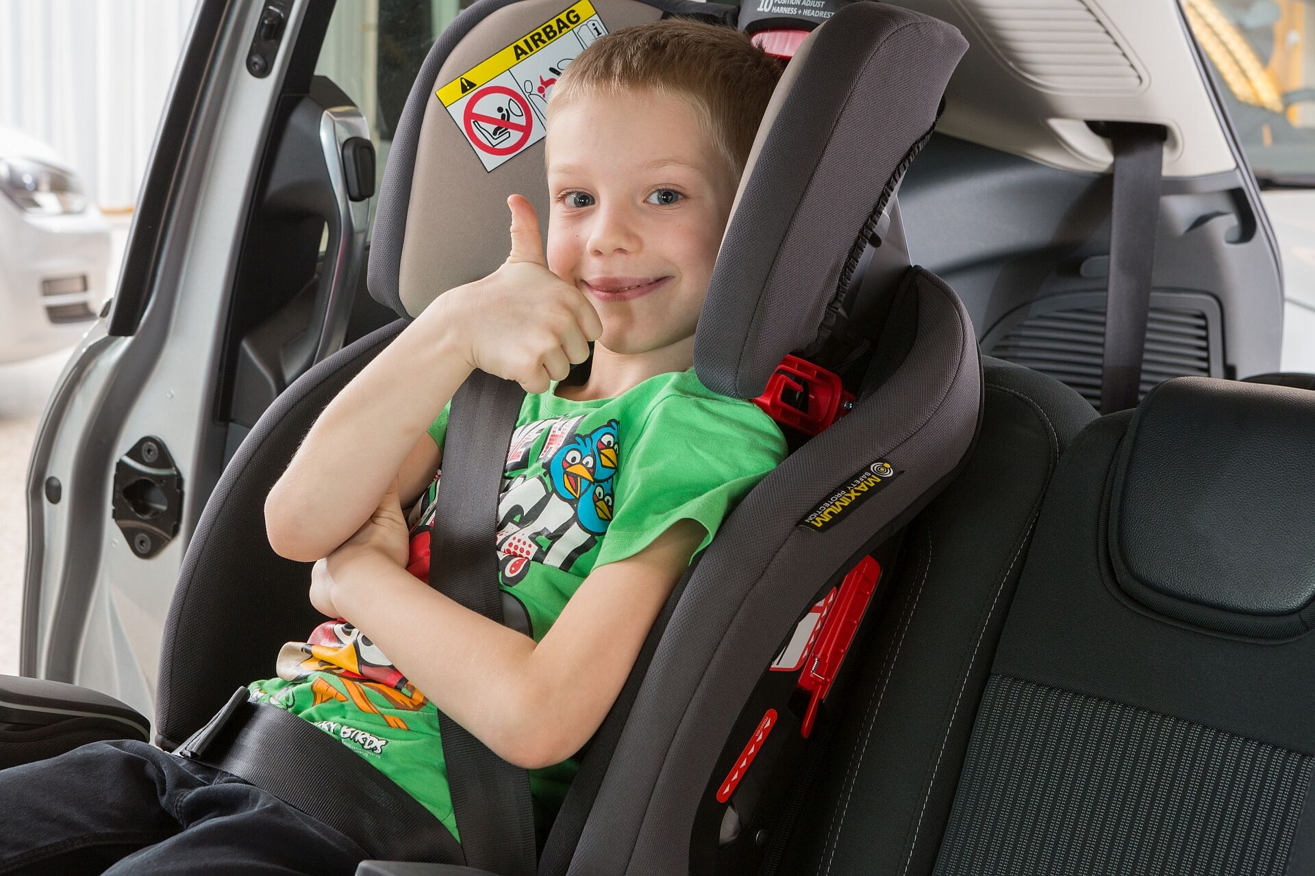 Ein Kind sitzt sicher im Kindersitz und hebt begeistert den Daumen nach oben, um seine Zufriedenheit und Sicherheit auszudrücken.