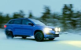 Winterreifentest 2022 - Auto  fährt auf Schneefahrbahn, im Hintergrund sieht man Bäume. Die Scheinwerfer sind eingeschaltet und leuchten den Weg vor dem Fahrzeug aus.