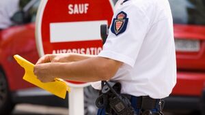 Polizist mit Strafzettel bei Verkehrskontrolle im Ausland vor Verkehrsschild und Auto